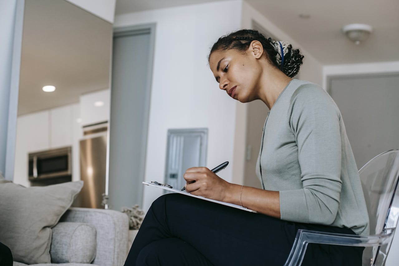 A focused woman writing on a clipboard, possibly a therapist in an office, reflecting professional concentration.