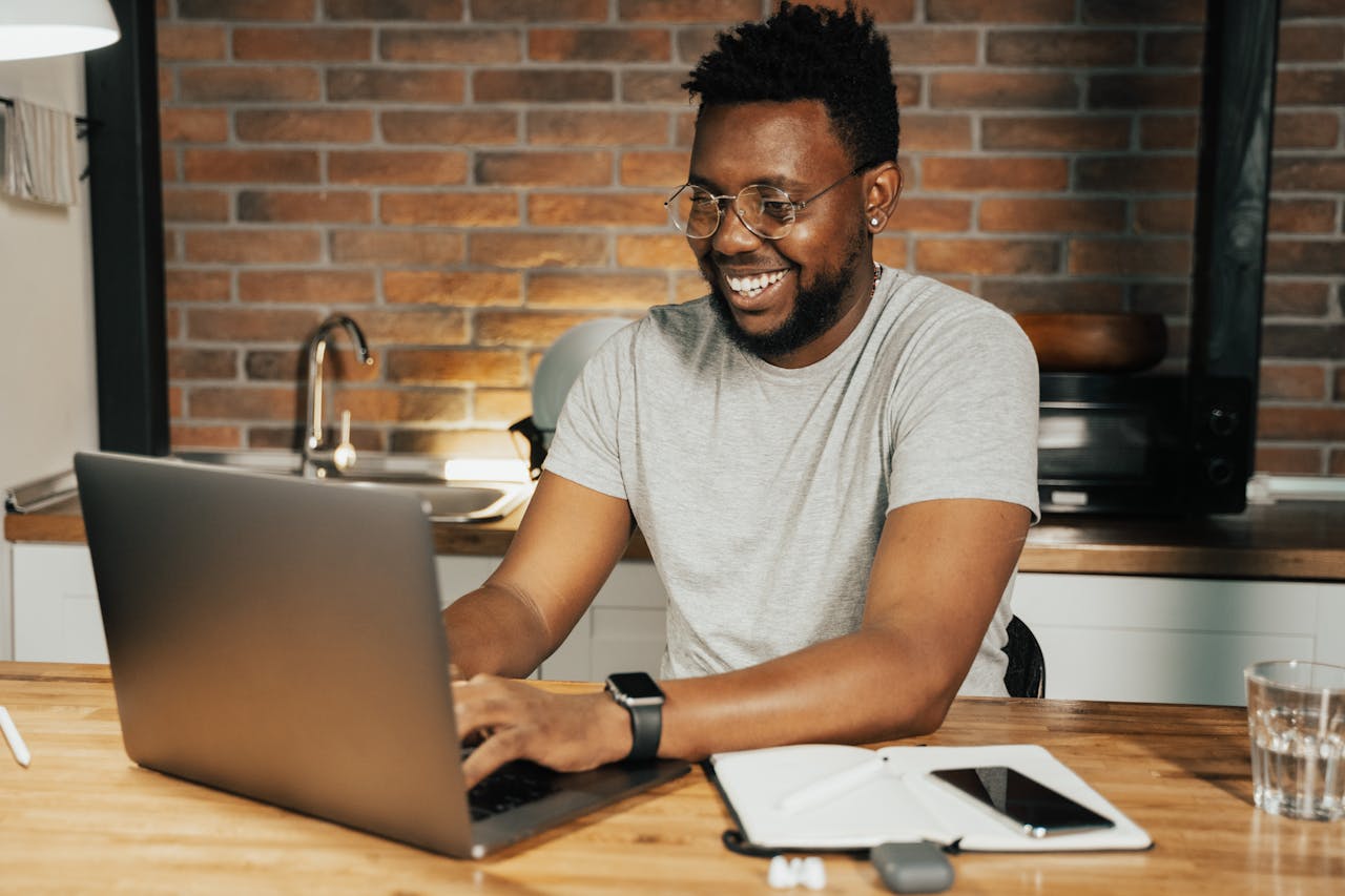 African American man smiling while working remotely on laptop from home office. Working on BFRBs in therapy.