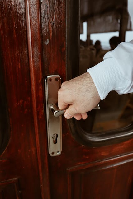 A close-up of a hand opening a textured wooden door with a brass handle.