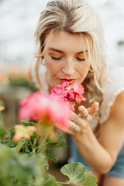 A woman inhales the fragrance of pink flowers in a serene setting, depicting calm and nature. Using 5 senses in I-CBT for OCD.