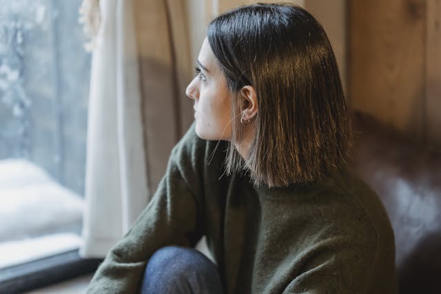 Thoughtful young woman gazing out a window, exuding serenity and contemplation.