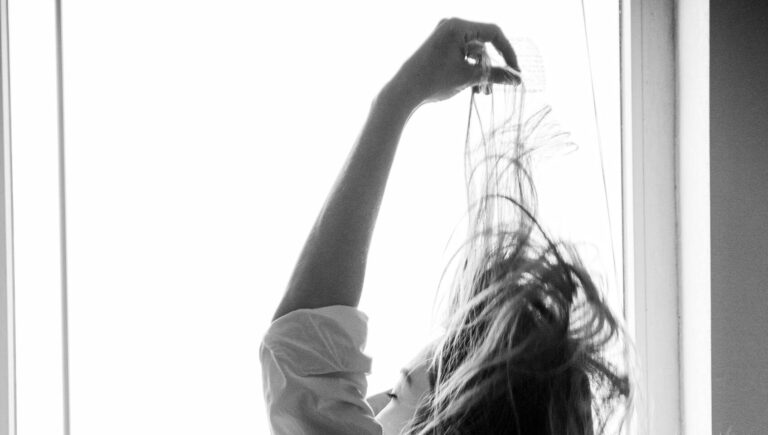 Black and white photo of a woman by a window holding a cup, capturing morning relaxation.